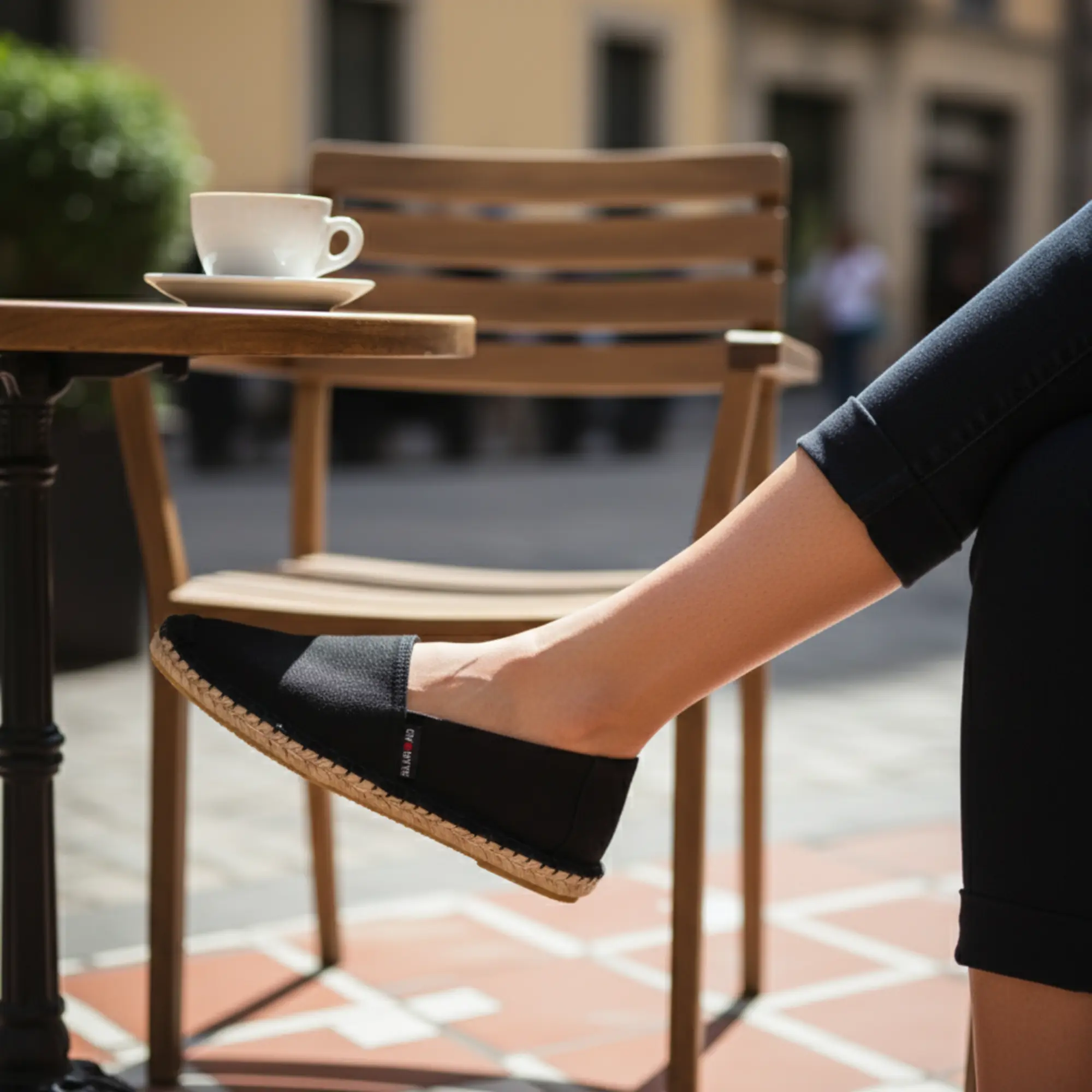 Frau mit schwarzen Espadrilles von Doubleface in einem Straßencafé.