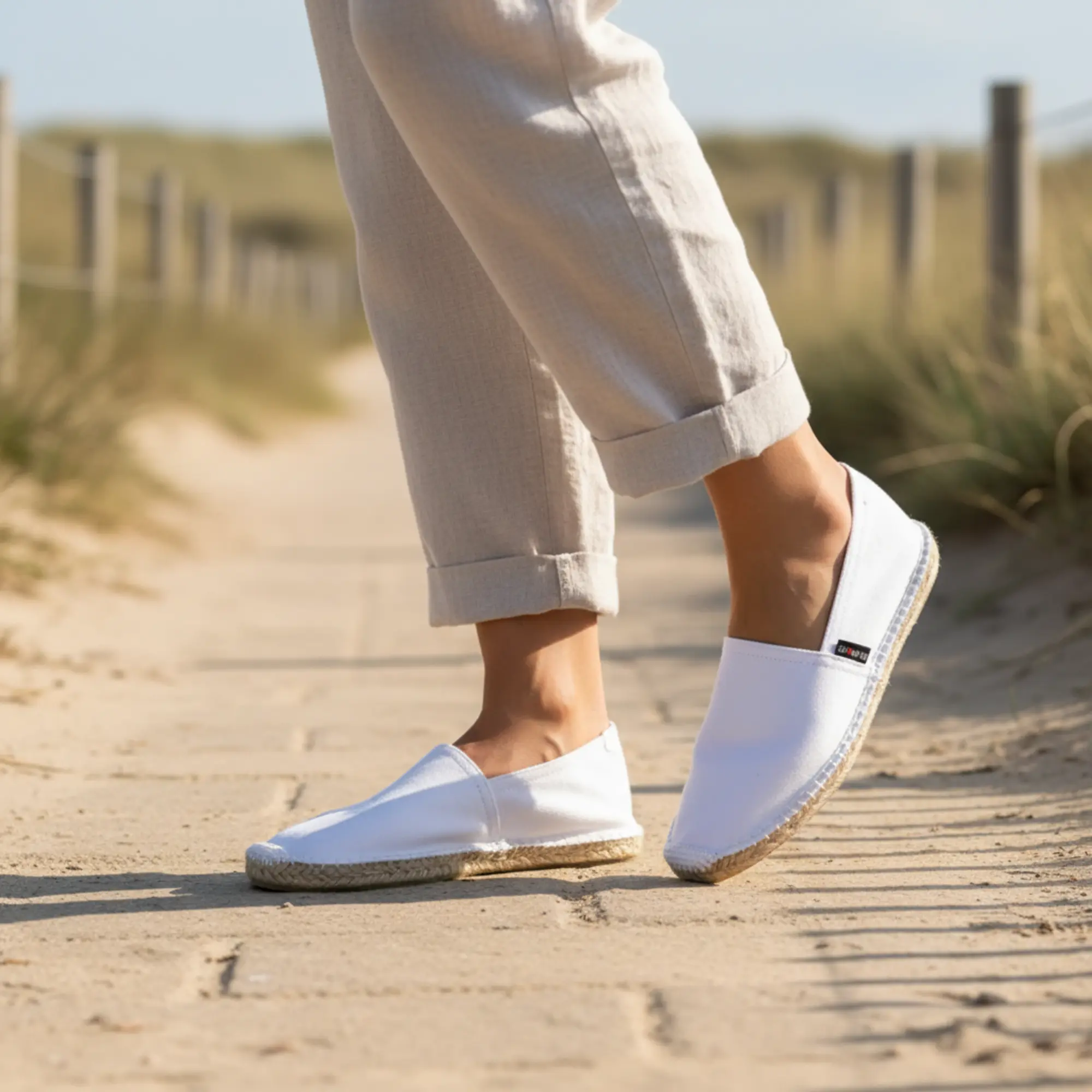 Person in weißen Espadrilles auf sandigem Holzsteg