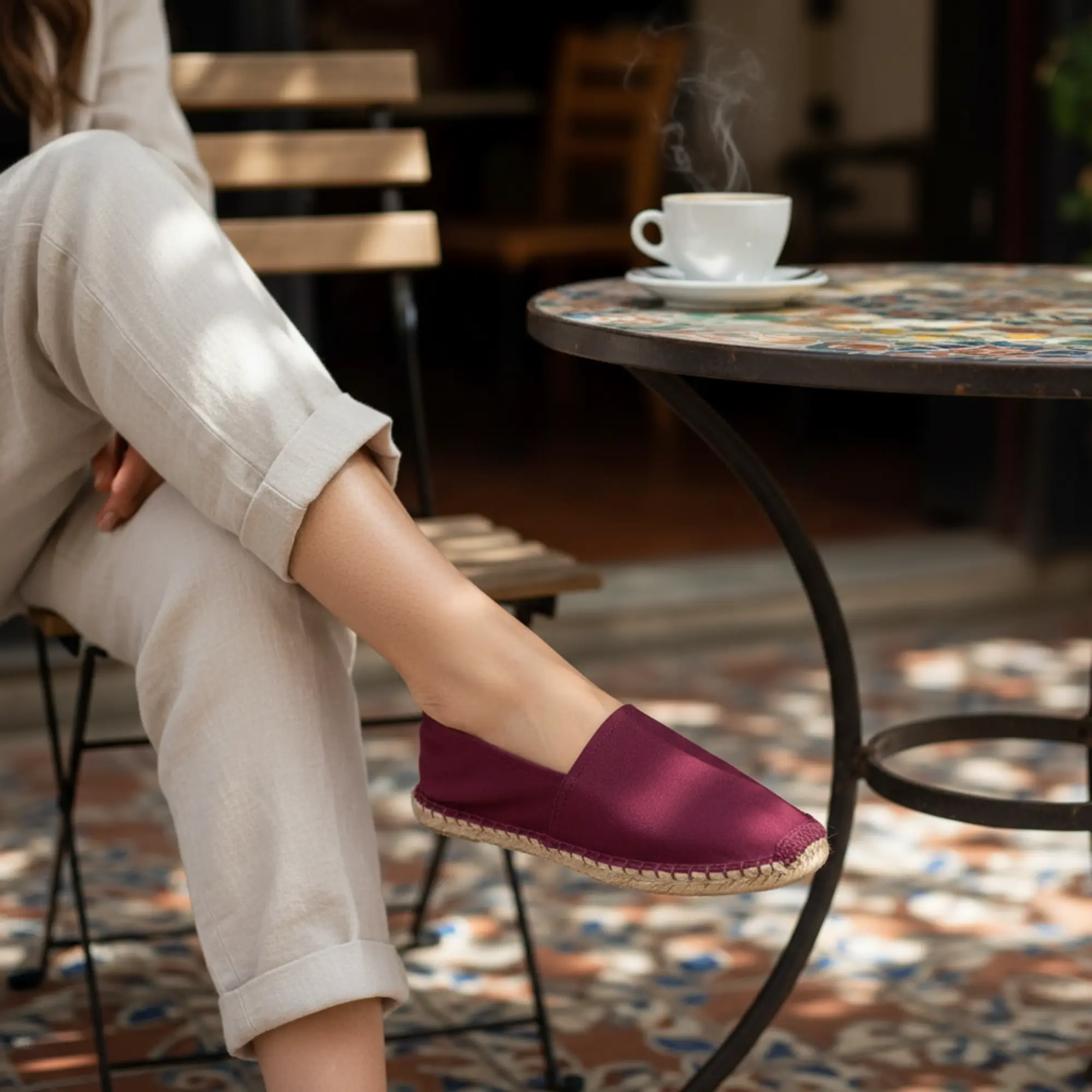 Frau mit bordeauxroten Espadrilles in einem Straßencafé.