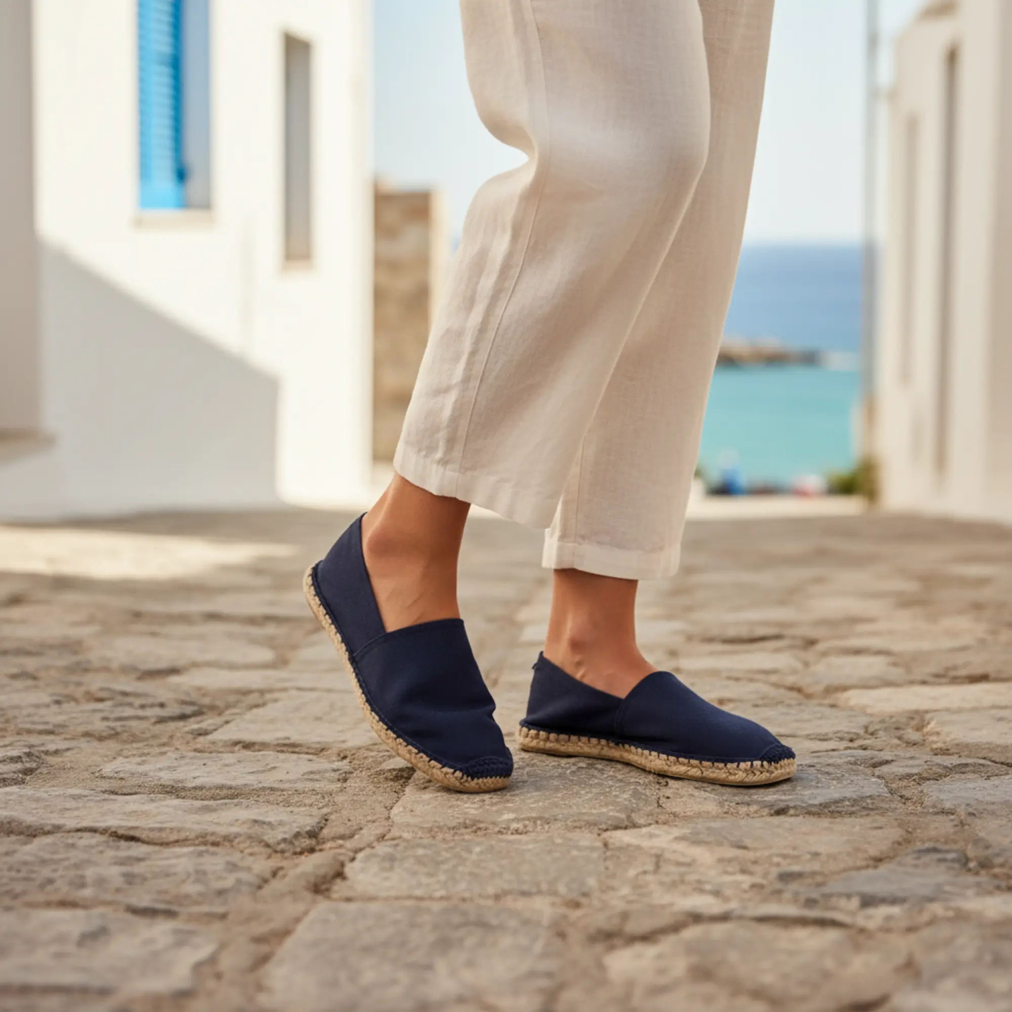 Marineblaue Espadrilles, Segeltuchhosen, Kopfsteinpflasterstraße in Griechenland.