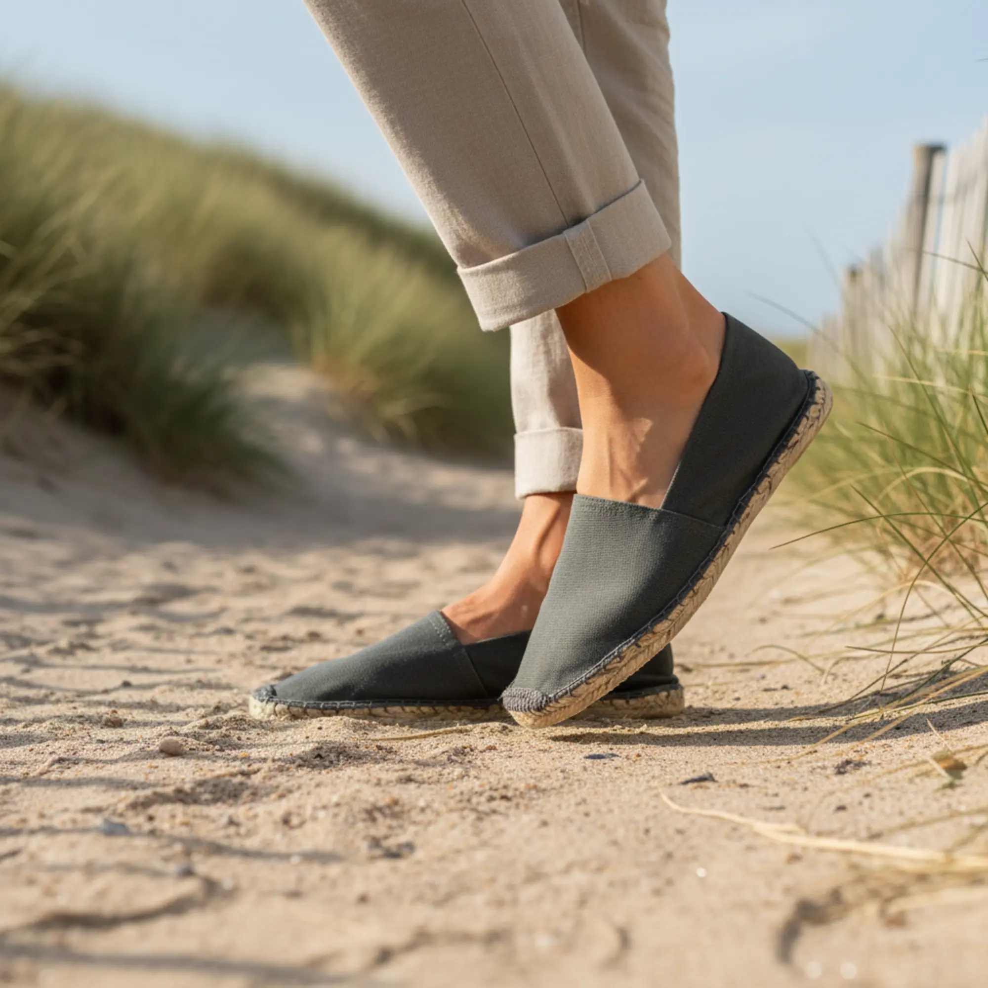 Person in dunkelgrauen Espadrilles am Strand.