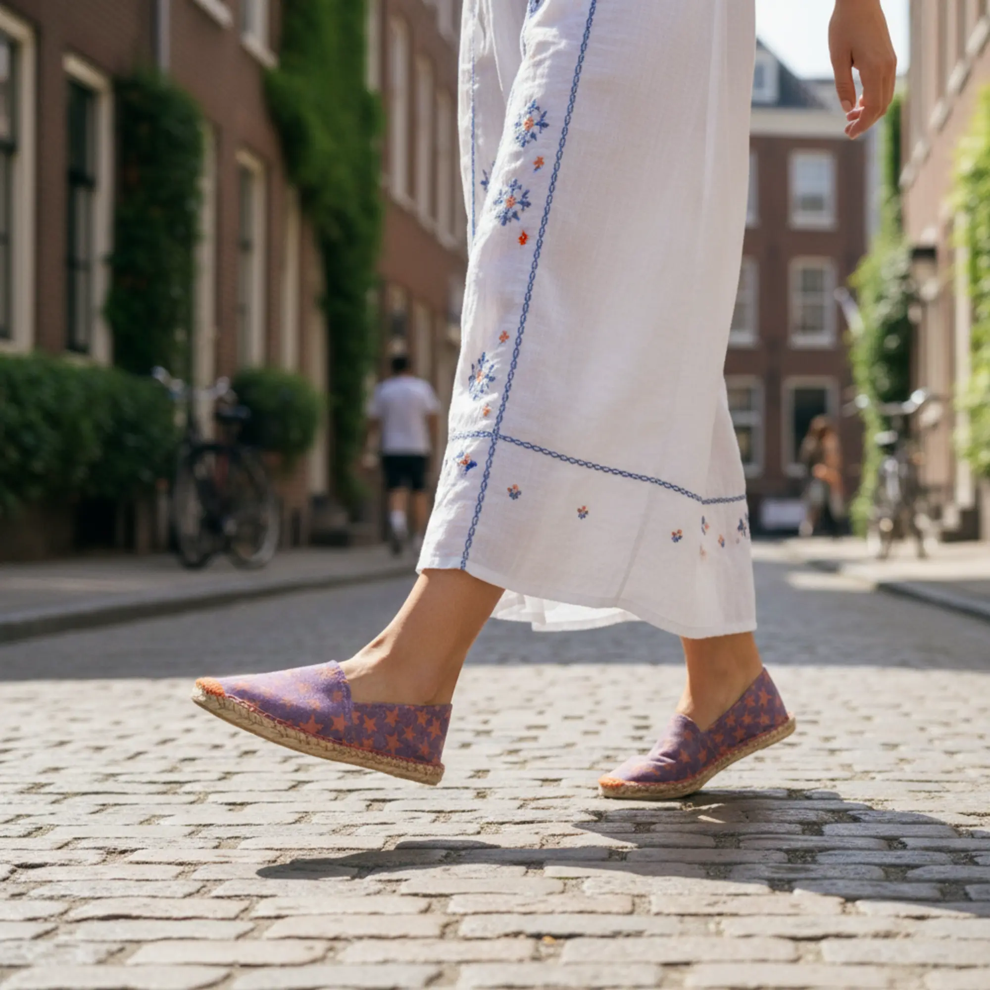 Eine Person geht in lila Espadrilles mit Sternenmuster auf Kopfsteinpflaster.