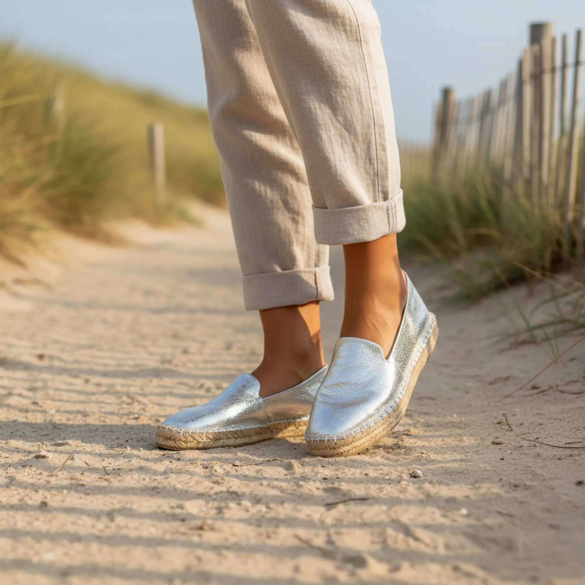Silberne Espadrilles auf einem sandigen Pfad, im Hintergrund Dünengras.