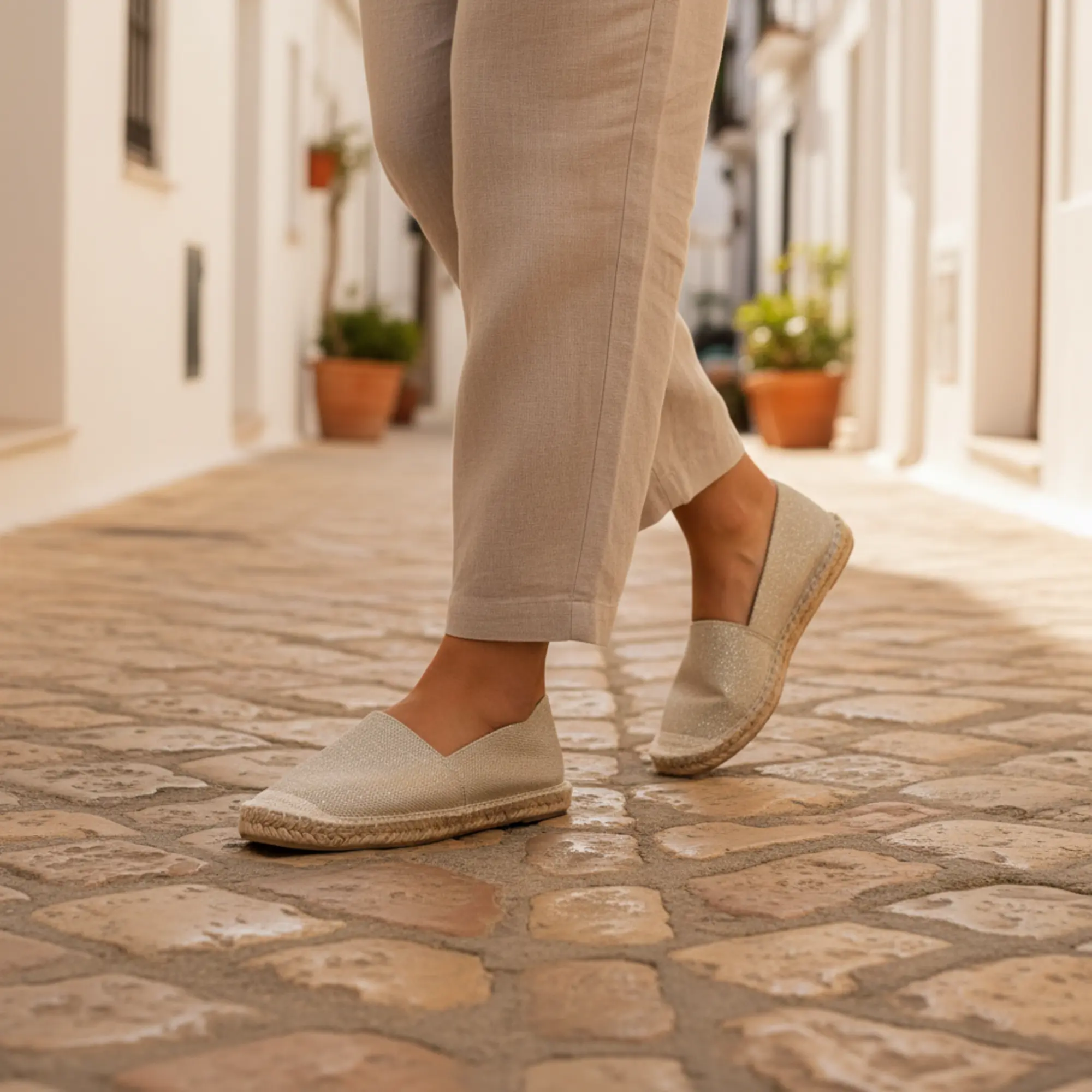 Frau in goldenen Espadrilles auf Kopfsteinpflaster.